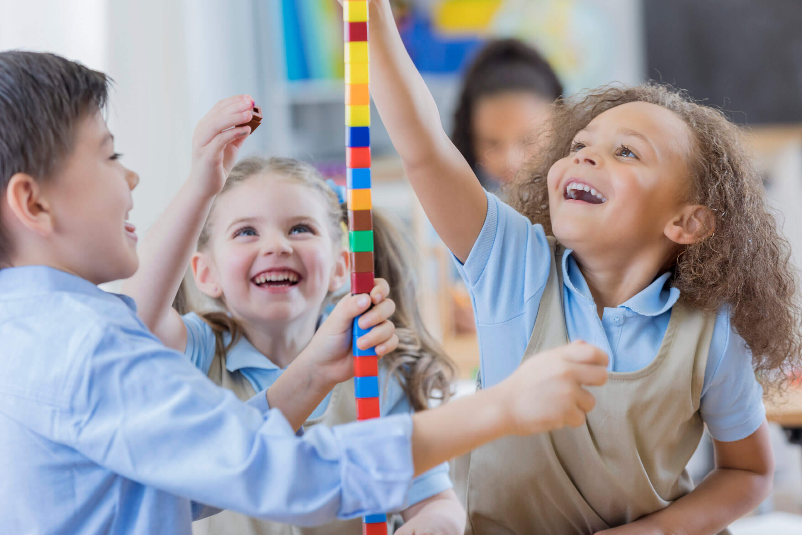 Excited young preschool students build a tower from counting cubes in their classroom.